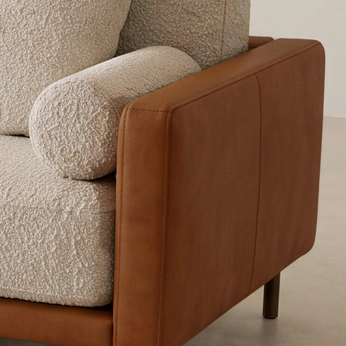 Close-up of the leather arm and round bouclé bolster on the Sella sofa