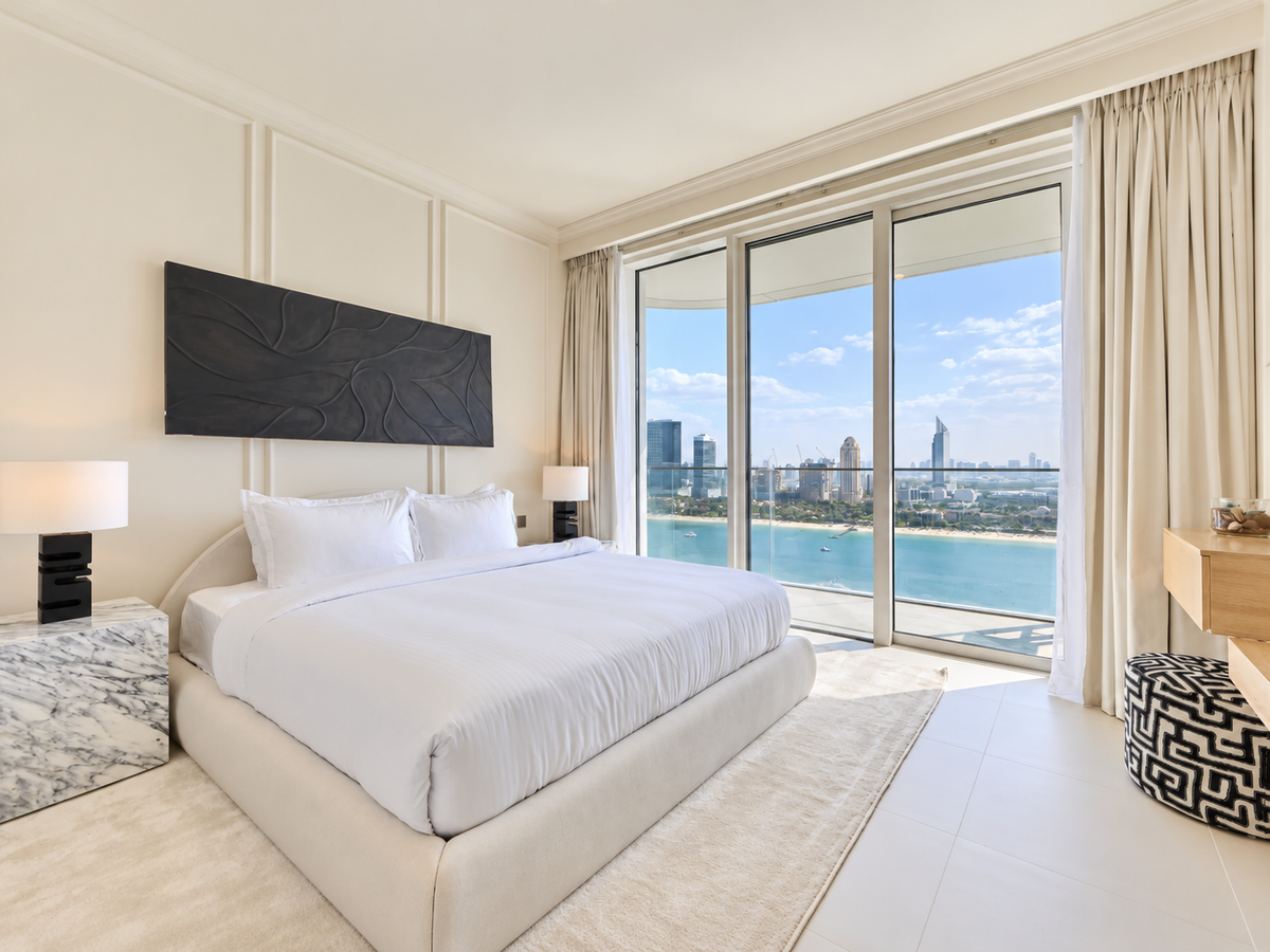 Custom curved white upholstered bed with a marble cube bedside table and sea view