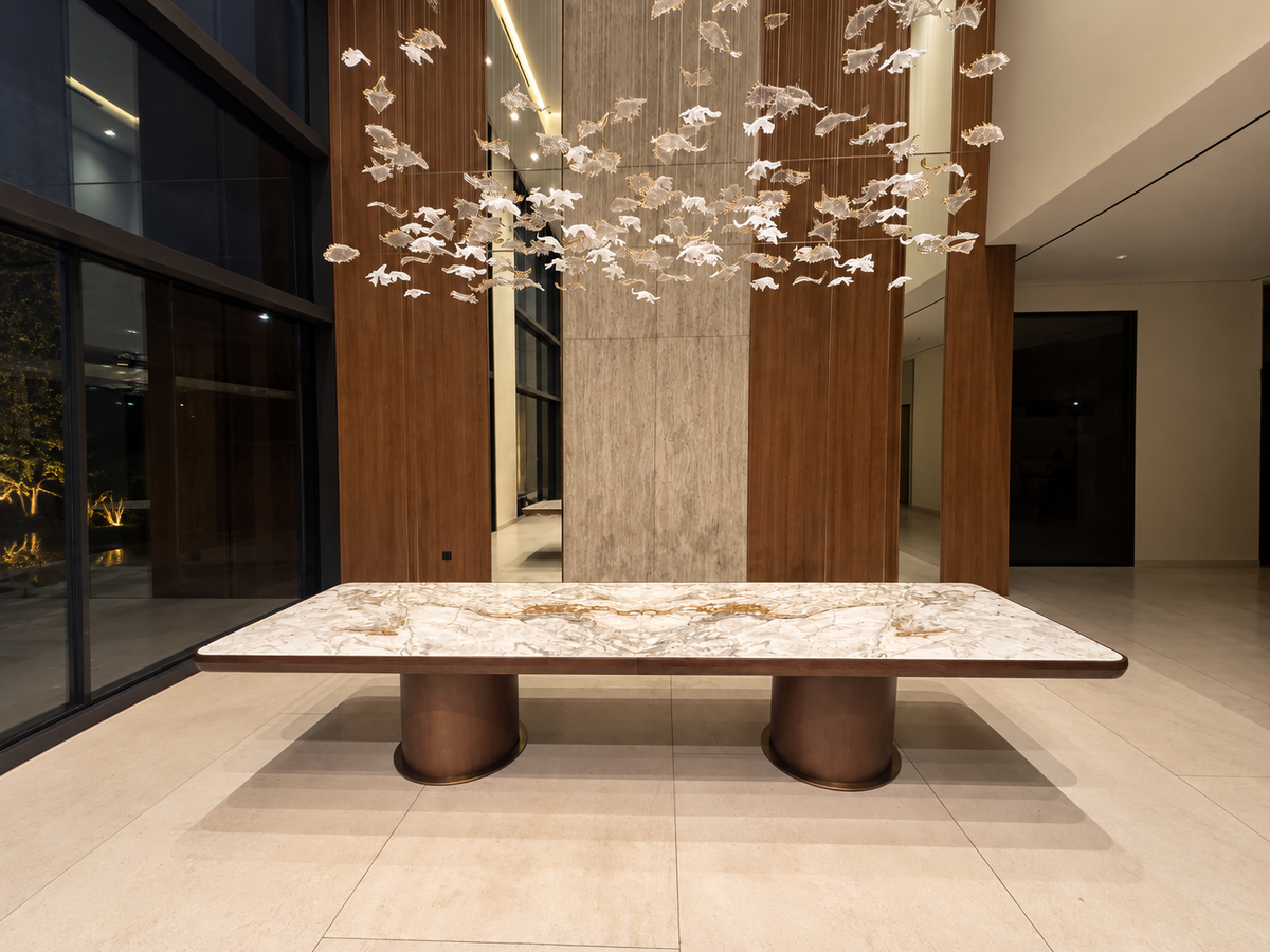 Custom marble and walnut dining table on twin pedestal bases beneath a glass sculpture