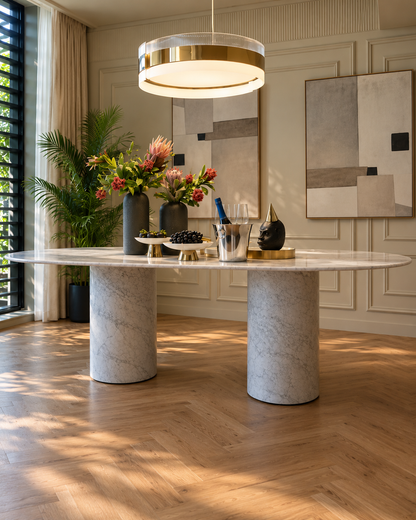 Impero oval dining table in white Carrara marble on two cylindrical marble columns in a dining room with a brass pendant light