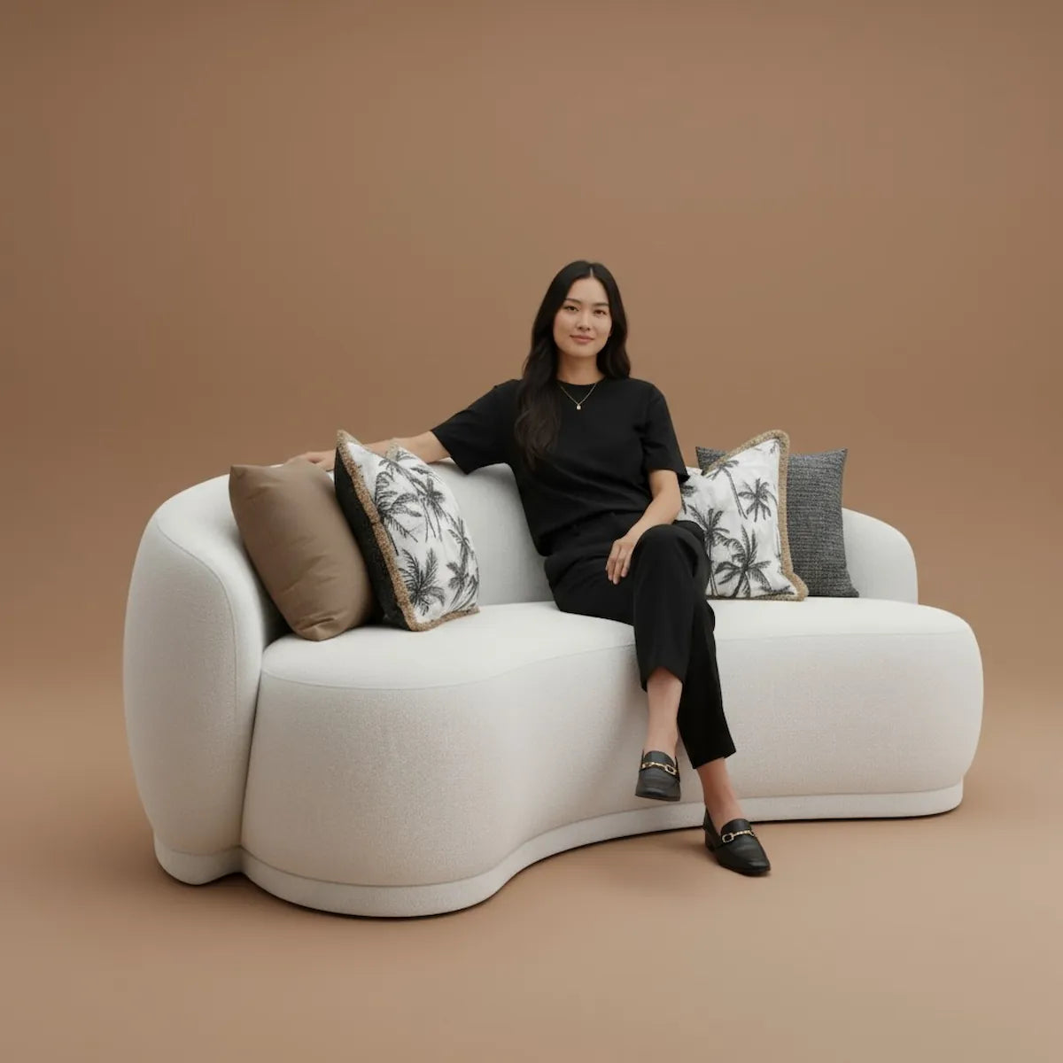 Casa Di Andi Mira Curved Sofa in off-white, styled in a warm living space with a person seated, highlighting comfort and design.